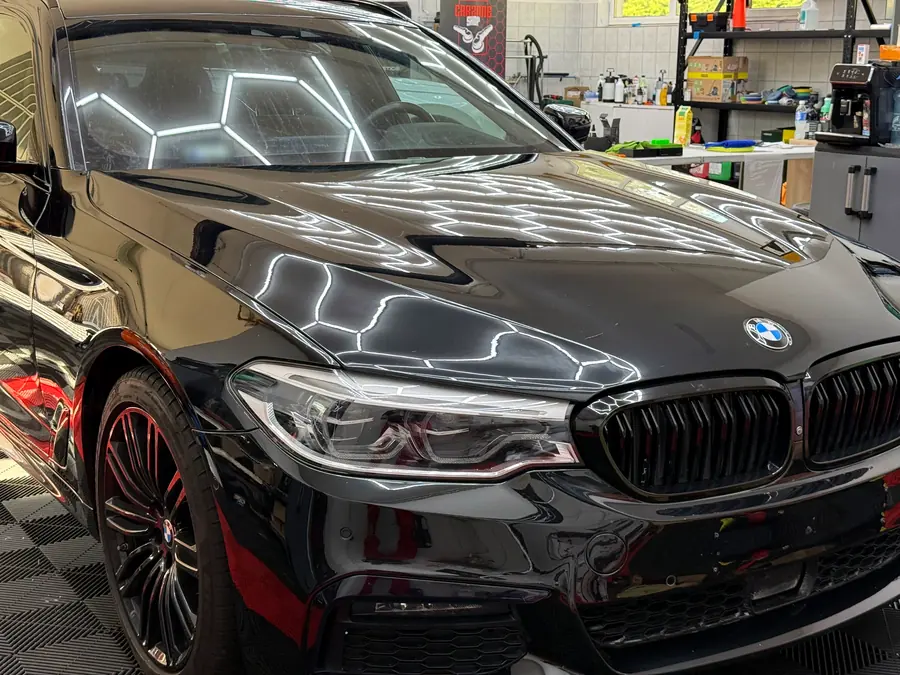BMW 5-ös sorozat fényszórója kővédő fóliázás után, a stúdió hatszög-lámpáinak tükröződésével